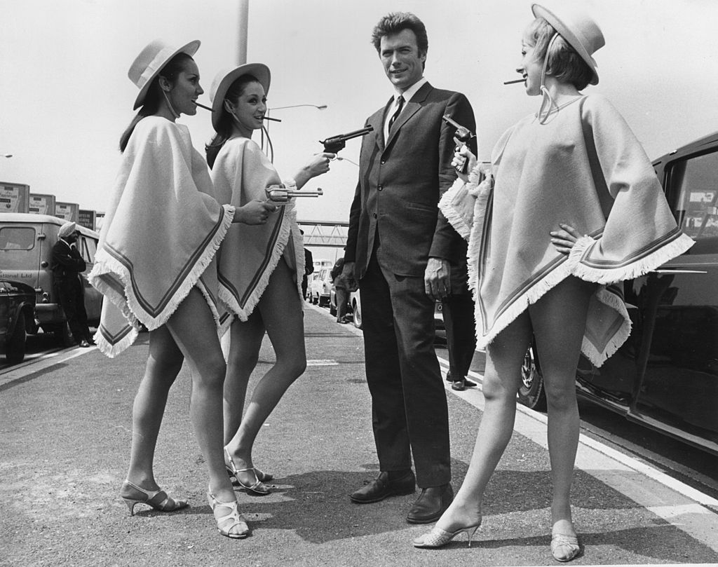 1st June 1967:  American actor Clint Eastwood finds himself at the mercy of three gun-toting gals upon his arrival at London Airport to promote his latest film. From left to right, the bare-legged banditos are Sandra Marshall, Anita McGregor and Susan Melody.  (Photo by Central Press/Getty Images)